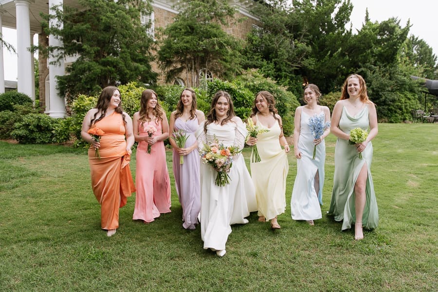 Bride walking across the lawn with bridesmaids in colorful dresses at Gassaway Mansion.