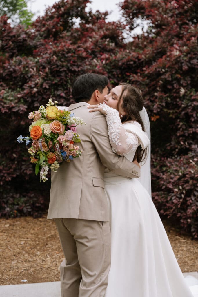 Newly married couple embracing outdoors after their wedding ceremony while holding a colorful bridal bouquet.