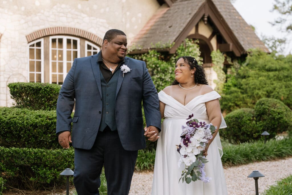 Newly married couple walking through the gardens of a Georgia wedding venue surrounded by landscaping and architectural details.